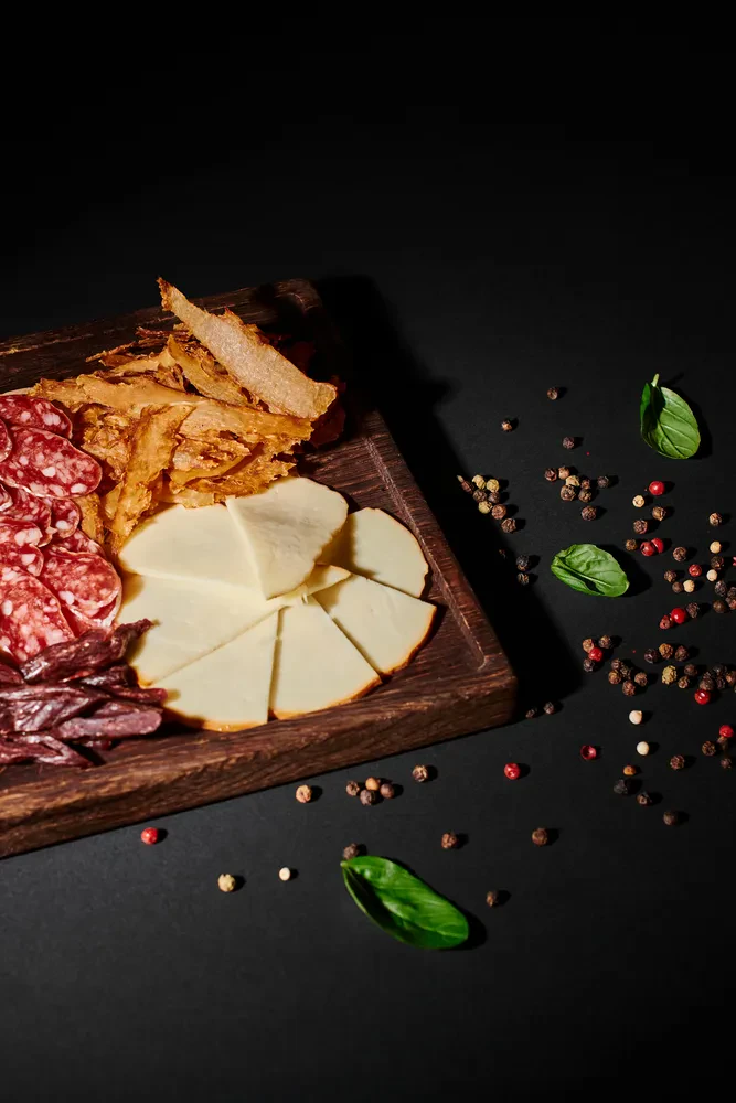 Privlačna mesna plošča z narezano sušeno govedino, rezinami salame in raznovrstnimi siri, servirana na temni podlagi.