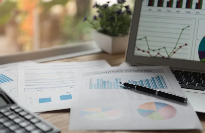 Finančno poročilo in grafi na mizi poleg kalkulatorja, kar prikazuje temeljito pripravo in analizo podatkov, ključnih za poslovno svetovanje.