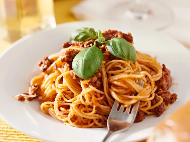 Klasični špageti z bogato mesno omako in lističi sveže bazilike, pripravljeni za uživanje. Odlična izbira italijanske kuhinje.