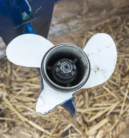 Od blizu je prikazan poškodovan aluminijast propeler izvenkrmnega motorja z zlomljeno lopatico, kar nakazuje na nujno potrebo po popravilu ribiške opreme v regiji Goriška.