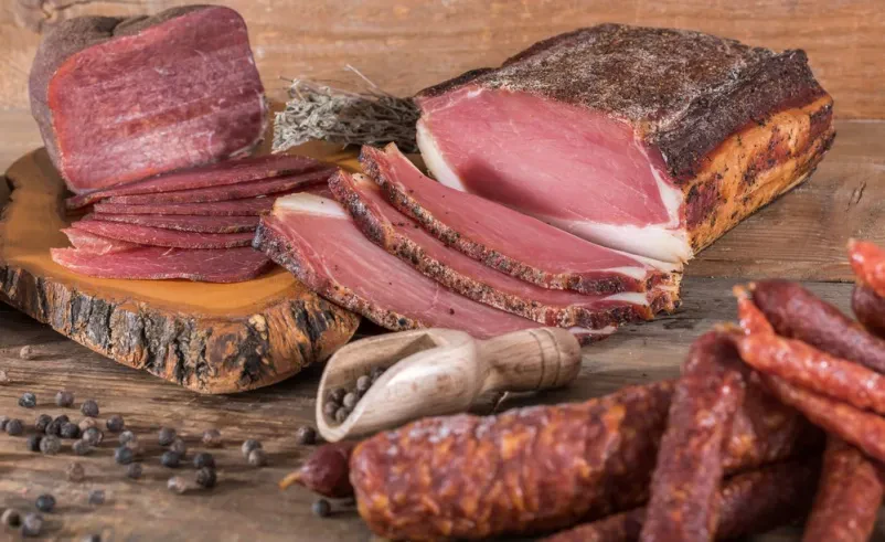 Različne dimljene mesnine in klobase Raznolikost dimljenih mesnin in klobas, ki so skrbno položene na rustikalni leseni površini. Predstavlja tradicionalno pripravo.