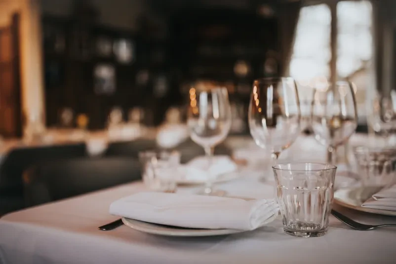 Bližnji posnetek restavracijske mize, postavljene z elegantno posodo in kozarcem za vino, pripravljene za goste.