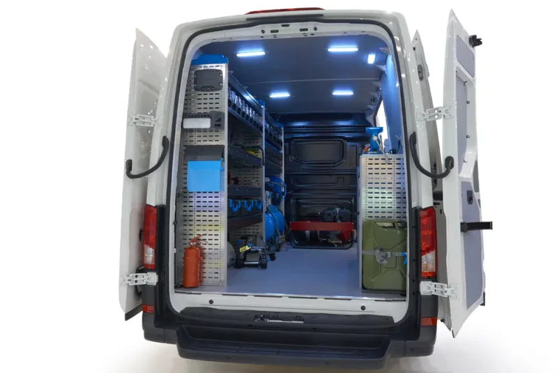 Mobilni servisni kombi Zadnji del specializiranega servisnega kombija, opremljenega za avtomehanična popravila in pomoč na cesti, prikazan na belem ozadju.