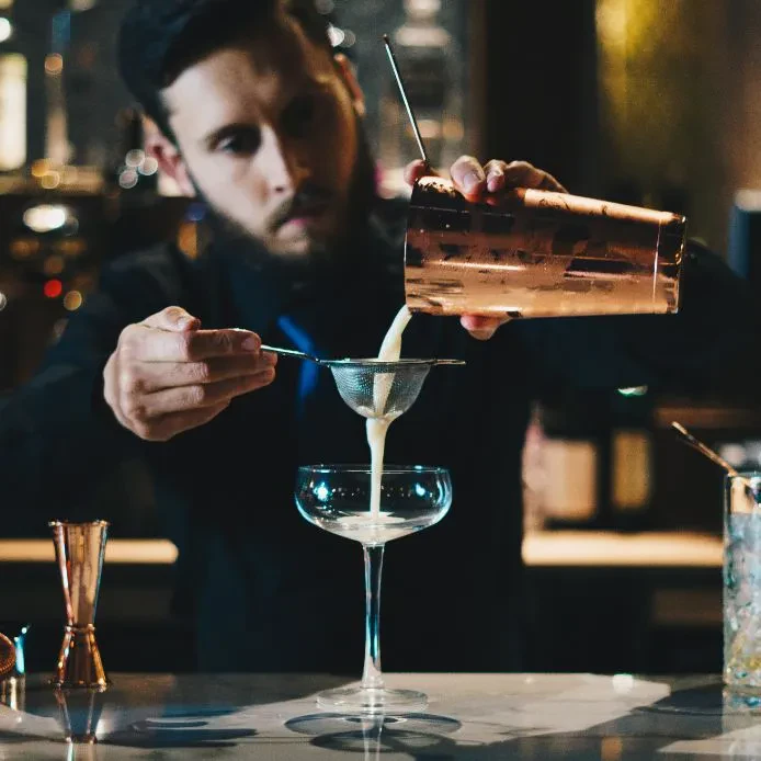Barmen s pijačo v roki med tečajem gastronomije Mladi barmen s ponosom pripravlja koktajl. Prikazuje praktično znanje gastronomije v Strokovni izobraževalni center Celje.
