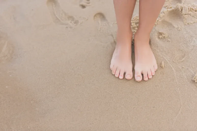 Otrok stoji na peščeni plaži ob morju. Ta prizor prikazuje mirne družinske počitnice in brezskrbno otroštvo, idealno za nastanitev blizu obale.
