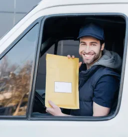 Nasmejan kurir znotraj dostavnega vozila drži paket in je pripravljen za nadaljevanje poti, kar poudarja mobilnost storitve.