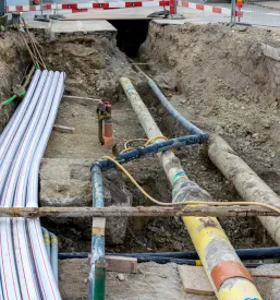 Velike komunalne cevi in kabelski kanali, položeni v odprt jarek na gradbišču, kjer se izvajajo infrastrukturna dela.