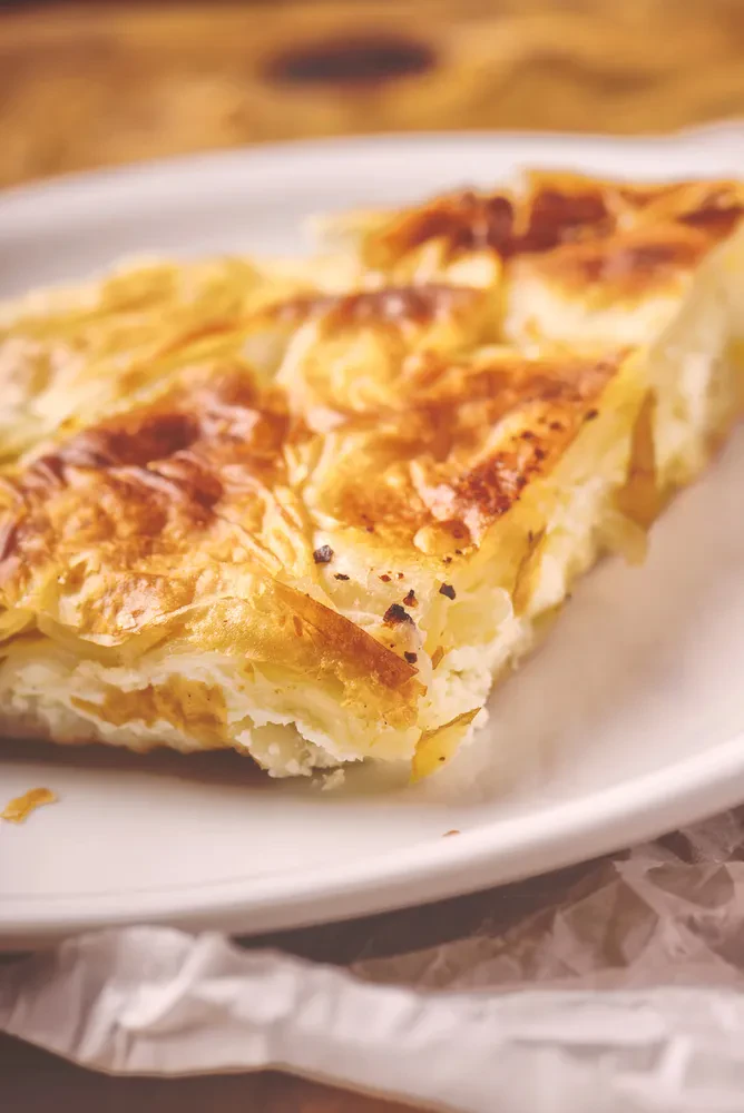 Burek s sirom, tradicionalna balkanska jed Okusen kos balkanskega bureka s sirom, ki je pravkar vzet iz pečice in pripravljen za uživanje. Hrustljav, zlate barve in dišeč.