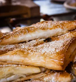 Več kosov hrustljavega bureka s sirom, posutega s sezamom, elegantno postreženi na krožniku. To je res dober burek Komenda, primeren za malico.