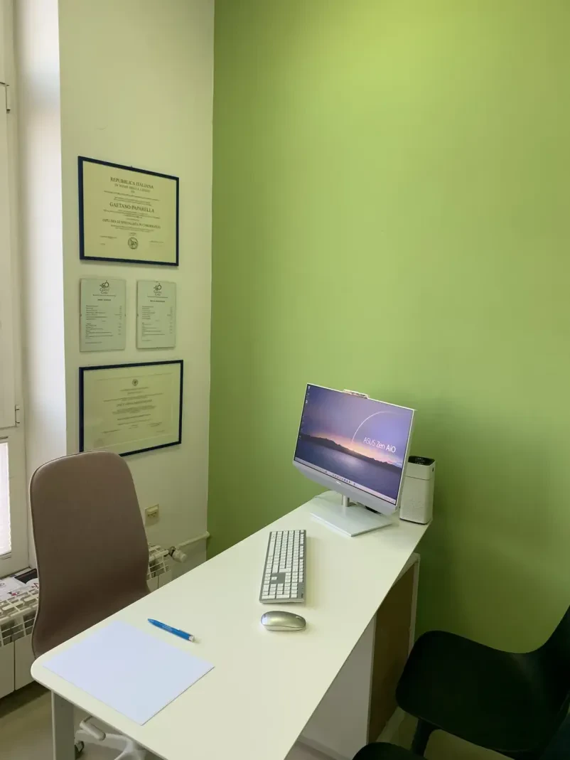 Kardiolog, oblečen v belo haljo, osredotočeno pregleduje podatke na računalniškem zaslonu v ordinaciji.