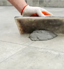 Keramičar zapolnjuje fuge med keramičnimi ploščicami z gumijasto gladilko, s čimer dokonča polaganje in zagotovi estetski videz.