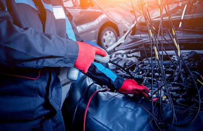 Mehanik med popravilom motorja Izkušen mehanik natančno pregleduje in popravlja motor avtomobila v delavnici, zagotavljajoč zanesljiv avtoservis.