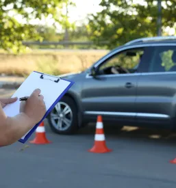 Od blizu posnetek moškega izpraševalca, ki drži beležnico med ocenjevanjem kandidata na poligonu za vožnjo.