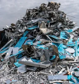 Prostrano dvorišče z velikimi kupi rjastega jekla in železa, ki pričajo o industrijski zgodovini in čaka na ponovno uporabo materialov.