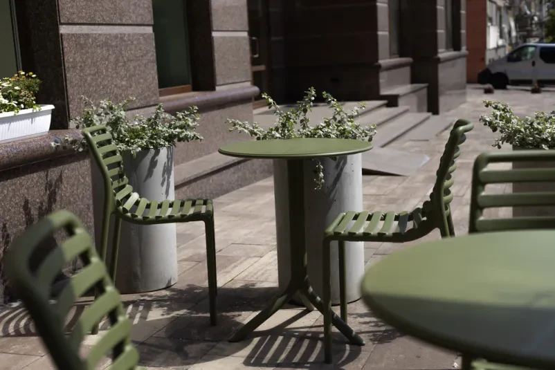 Prazna letna terasa kavarne s stoli in mizami Udobni stoli in mize na prostorni letni terasi, pripravljeni za obiskovalce, ki želijo uživati v poletni odprti kavarni Domžale.