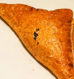 Zlato-rjavi trikotni slani žepki s piščančjim nadevom, posuti s črnim in belim sezamom, so postreženi na preprostem belem keramičnem krožniku.