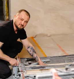 Gradbeni delavec spretno reže keramično ploščico z ročnim rezalnikom, ključen korak pri prilagajanju za brezhibno vgradnjo v prostor.