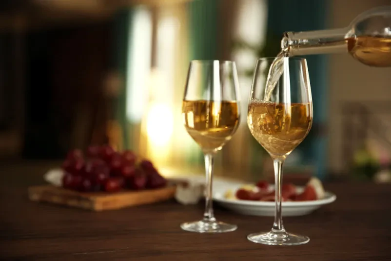 Prijeten prizor nalivanja svežega belega vina iz steklenice v kozarec, pripravljenega za pokušino. Idealno za prodajo belega vina Pomurska, kjer cenimo kakovost in tradicijo.