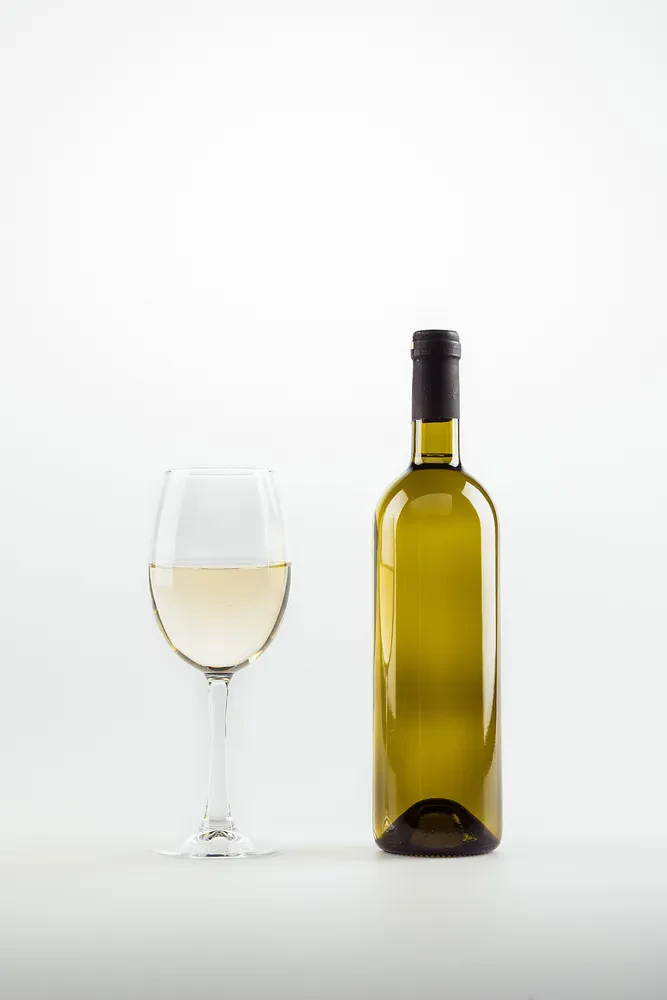 Bližnji posnetek kozarca in steklenice belega vina, elegantno postavljenih na belem ozadju. Prikazuje preprostost in eleganco ob vsaki priložnosti.