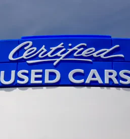 Velik moder napis 'Certified Used Cars' stoji pred avtosalonom in poudarja ponudbo preverjenih rabljenih vozil za zanesljiv nakup.