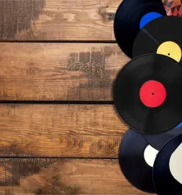 Skrbno urejena zbirka starih vinilnih plošč, ki ležijo na leseni površini, v retro stilu, pričara nostalgično vzdušje minule glasbene zgodovine.