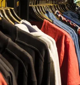 Barvite srajce in majice visijo na obešalnikih v sodobni trgovini, ki ponuja širok izbor oblačil za različne stile in priložnosti, poudarjajoč veliko ponudbo.
