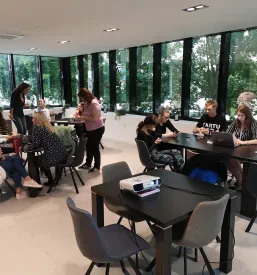 Velika skupina nasmejanih ljudi različnih starosti pozira za fotografijo na družabnem dogodku. Prikazuje močno skupnost in povezovanje.